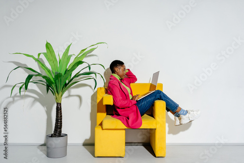 Female freelancer with laptop working in yellow armchair