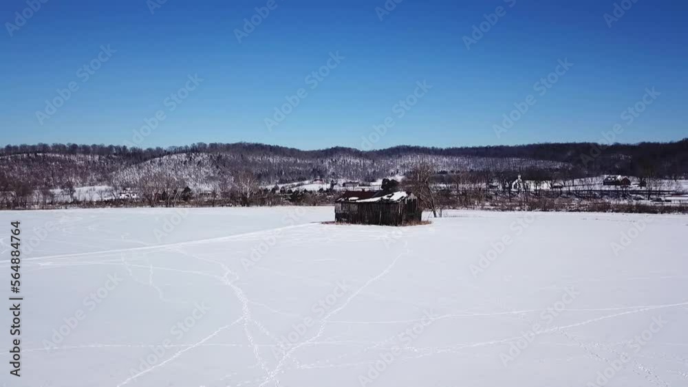 Slow dolly aerial moving towards a large abandoned, broken down, black barn during the winter with snow all over the ground and animal tracks visible Slow dolly aerial moving towards a large abandoned, broken down, black barn during the winter with snow all over the ground and animal tracks visible