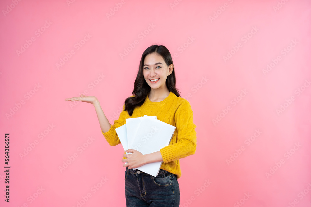 A smiling female student with long hair wearing a yellow coat and jeans. in hand a book on the pink background studio High school university college education. A smiling female student with long hair wearing a yellow coat and jeans. in hand a book on the pink background studio High school university college education.