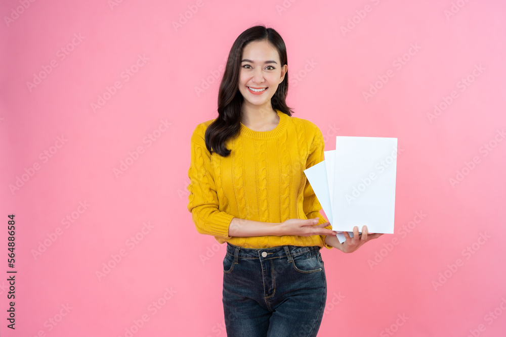 long haired female student Dressed in a yellow shirt, formal jeans, in her hand presents a white book. happy smile on the pink background studio High school university college education. long haired female student Dressed in a yellow shirt, formal jeans, in her hand presents a white book. happy smile on the pink background studio High school university college education.