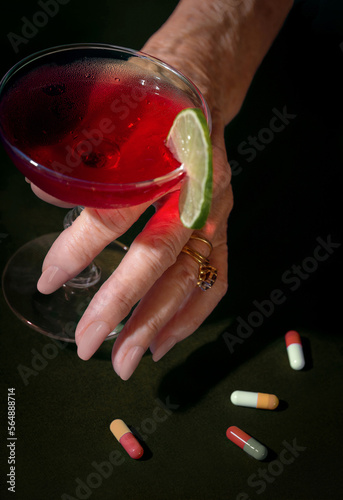 Woman Holds Alcoholic Beverage Next to Pills photo