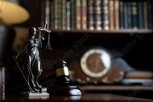 Law theme. Judge chamber. Judge’s gavel, Themis sculpture, scale and collection of legal books on the brown desk.