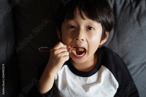 Little Asian boy, brushing his teeth on the sofa  photo