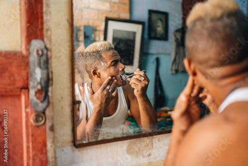 Cuban barber with razor shaving face in barbershop photo