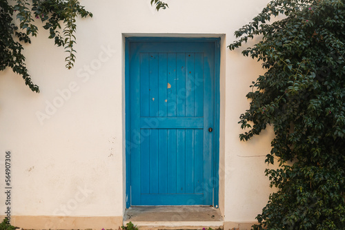 traditional white Greek house facade with blue door . Close-up of a wooden blue  dors and flower in a white stone building