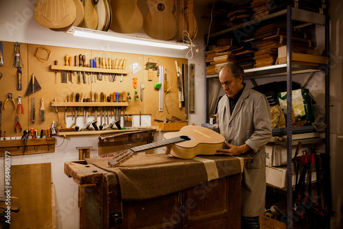 Focused luthier working in workshop with a classic spanish guitar