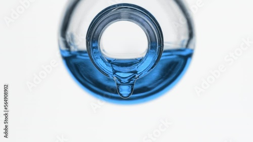 Side view macro shot of blue oil is dripping from reagent bottle on grey background | Abstract skin nutrition cosmetics ingredients formulating concept photo