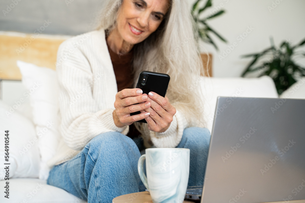 Mature woman at home with phone and laptop Mature woman at home with phone and laptop