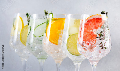 Gin tonic citrus cocktails set. Alcoholic drinks in wine glass with lime, lemon, grapefruit, orange, soda and herbs, gray background. Summer cocktail party. Close-up banner