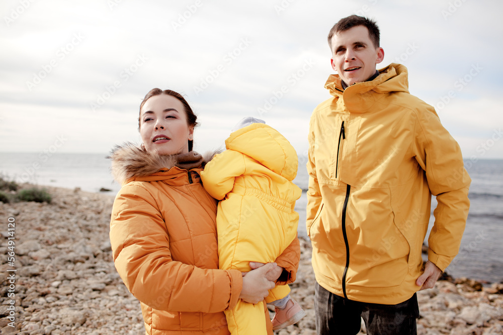 Happy multinational family walking in the beach with little kid tigether in cold weather against the background sea