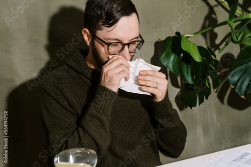 man blowing his nose at his desk