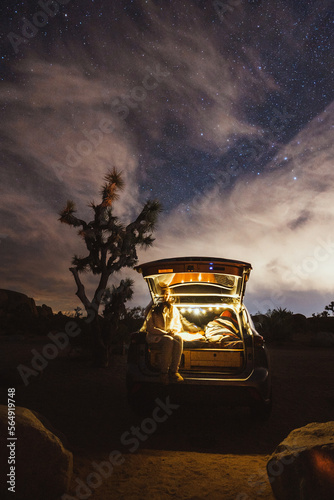 Woman Relaxing Under Night Sky In Joshua Tree With Car Camper photo