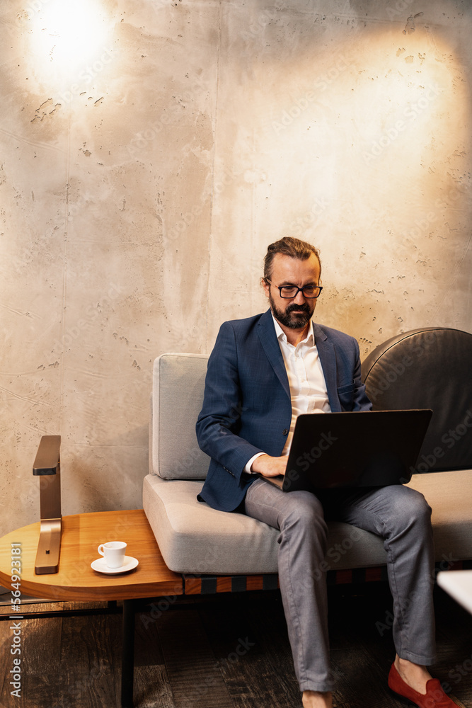 © Aleksandra Jankovic/Stocksy - Businessman In His 50s Sitting On The Sofa And Using A Laptop