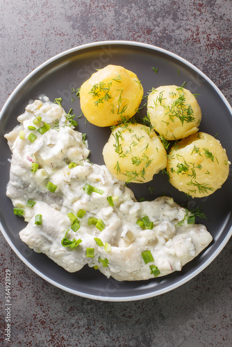 Sahnehering is a German dish with pickled Herrings fillets, apples and onion in a spiced marinade of cream served with boiled potato closeup on the plate on the table. Vertical top view from above