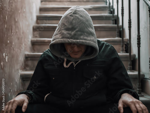 Tense man in hood sitting on stairs. Drug addiction or depressed person with problems.