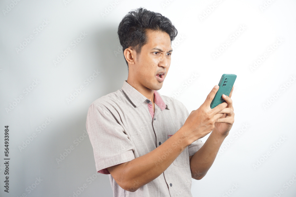 Amazed shocked asian guy holding smartphone in his hand, looking at the phone in surprise, stunned facial expression, stands on isolated white background Amazed shocked asian guy holding smartphone in his hand, looking at the phone in surprise, stunned facial expression, stands on isolated white background