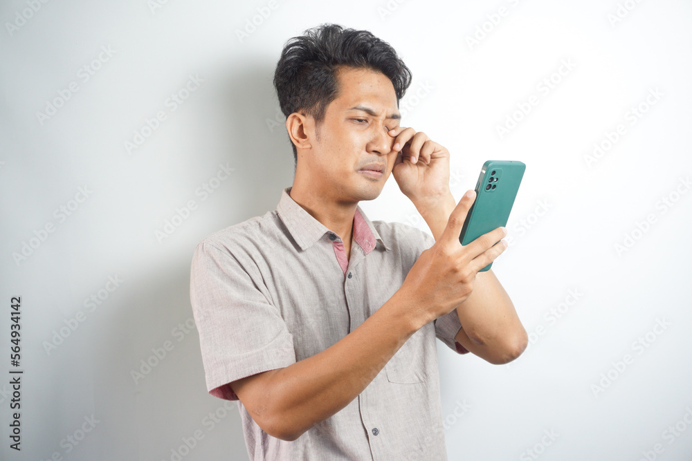 sad handsome asian man looking at notification on his cellphone sad handsome asian man looking at notification on his cellphone
