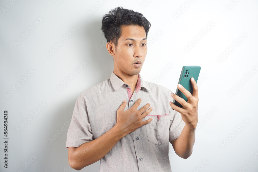 Amazed shocked asian guy holding smartphone in his hand, looking at the phone in surprise, stunned facial expression, stands on isolated white background Amazed shocked asian guy holding smartphone in his hand, looking at the phone in surprise, stunned facial expression, stands on isolated white background