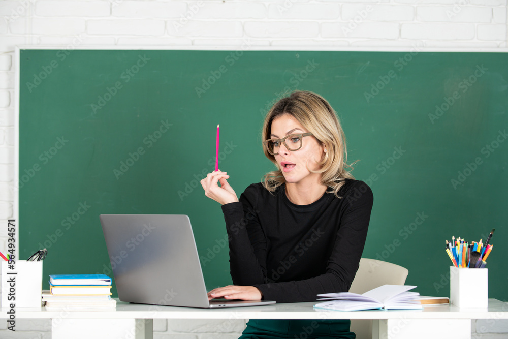 Modern attractive teacher. Portrait of smart young woman in glasses with book on the blackboard in class at high school or collage. Female professor at school, ready to start lesson. Modern attractive teacher. Portrait of smart young woman in glasses with book on the blackboard in class at high school or collage. Female professor at school, ready to start lesson.