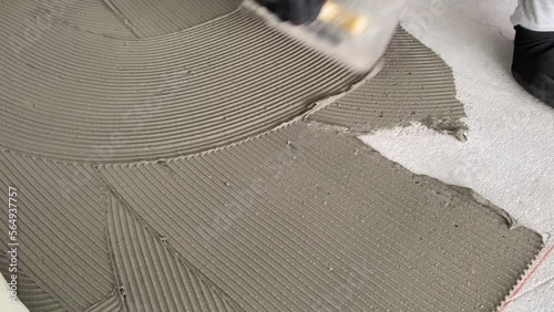 A builder applies tile adhesive to the floor. 4k video footage of construction work on laying tiles.