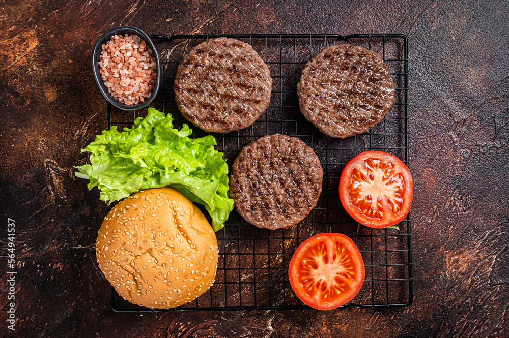 Grilled hamburger patties with tomatoes and seasonings on kitchen table. Dark background. Top view