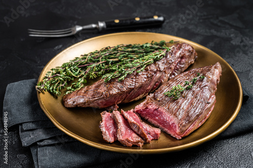 BBQ grilled Bavette Bavet beef meat steak with herbs on a plate. Black background. Top view