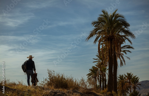 Rear view of adult man in cowboy hat walking on dirt road in desert. Almeria, Spain © WeeKwong