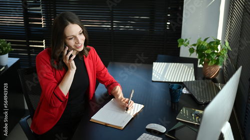 Attractive caucasian businesswoman in elegant red suit having pleasant conversation while sitting at workstation photo