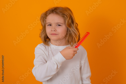Portrait of child combing hair with comb on yellow studio background. Tangled kids hair. Child with brush combing hair. Boy taking hairstyle. Child brushing hair with comb, kids haircare.