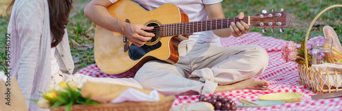 In love couple enjoying picnic time playing guitar in park outdoors Picnic. happy couple relaxing together with picnic Basket