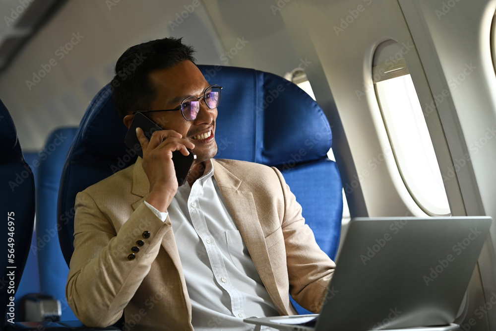 Successful businessman passenger talking on mobile phone while sitting in airplane cabin near windows Successful businessman passenger talking on mobile phone while sitting in airplane cabin near windows