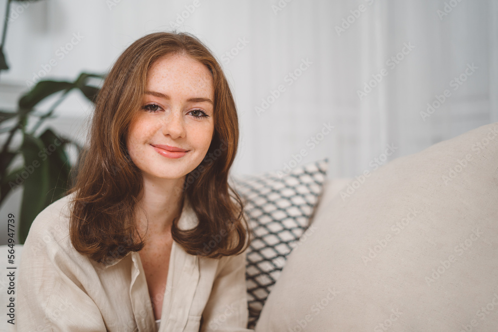 Portrait of beautiful cheerful redhead girl smiling looking at camera sitting on sofa at home Portrait of beautiful cheerful redhead girl smiling looking at camera sitting on sofa at home
