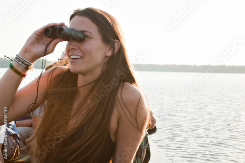 A young woman looks through binoculars at various types of birds on lake Sandoval in the amazon rainforest. photo