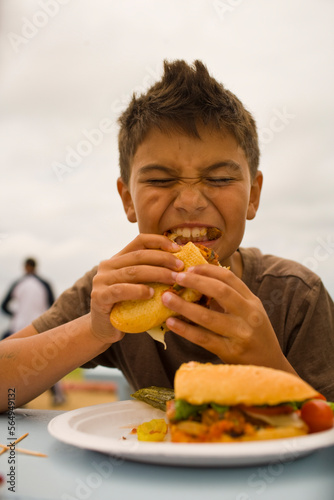 A young boy devours a sandwich at a picnic table, outdoors in California. photo