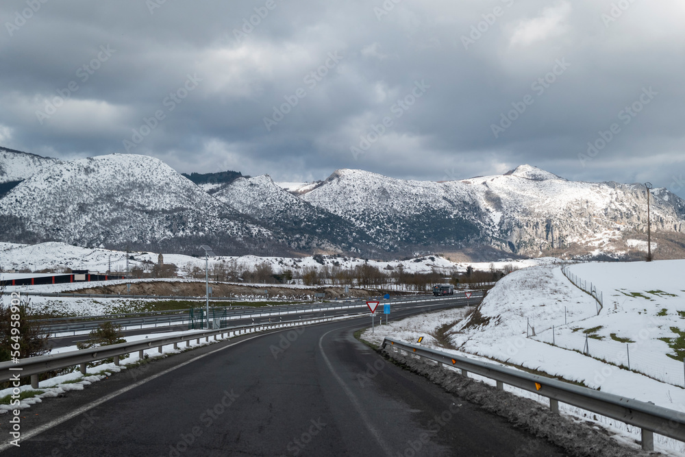 Estrada com uma curva de acesso à autoestrada num dia frio de inverno com muita neve e com montanhas ao fundo também cobertas de neve em Espanha