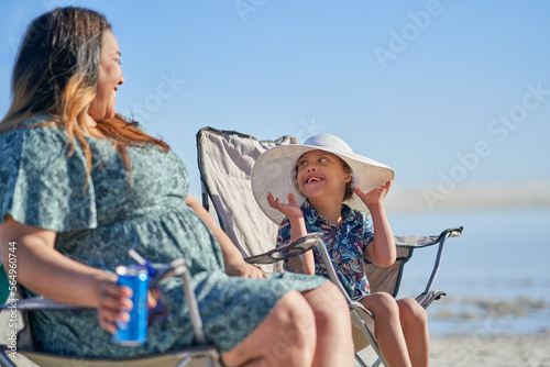 Mother watching happy cute son with Down Syndrome in hat on beach