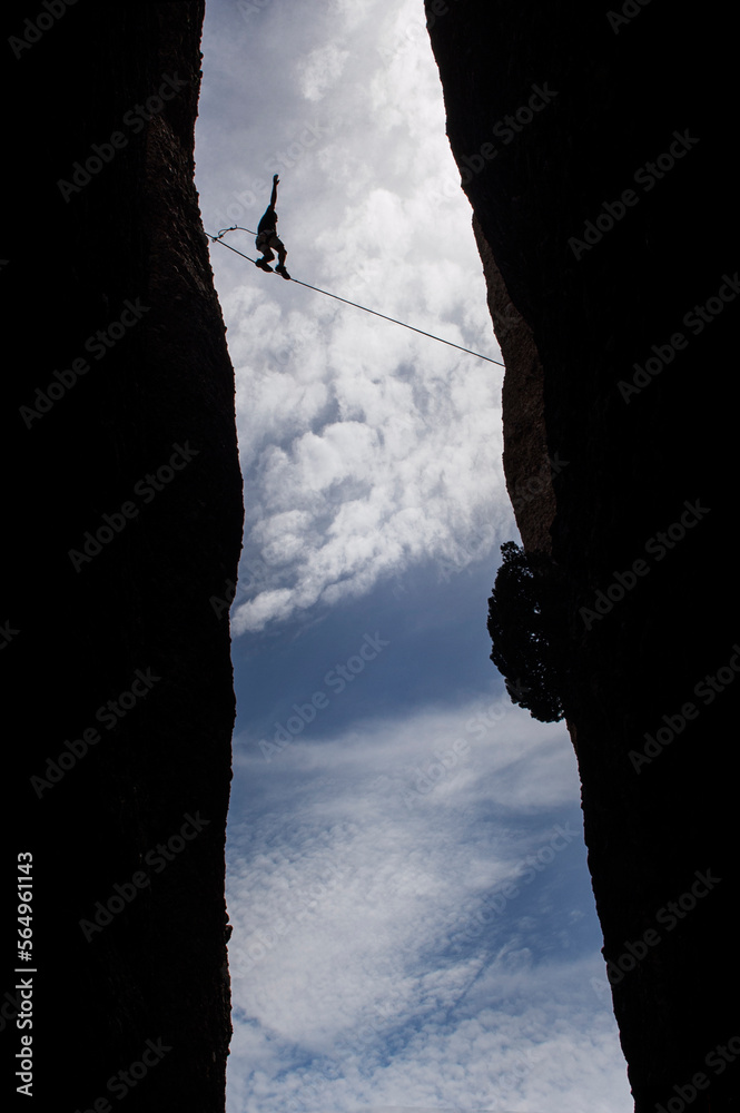 Silhouette of young man balancing on slackline, between two mountains