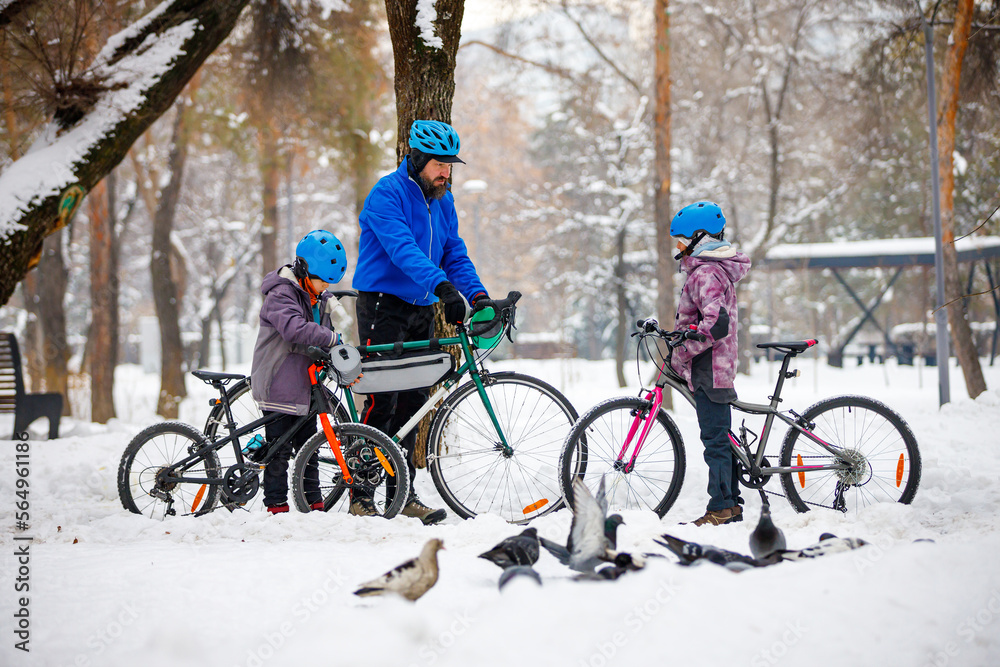 A man with his son and daughter ride bicycles in a winter park. Father with children. Winter weekend
