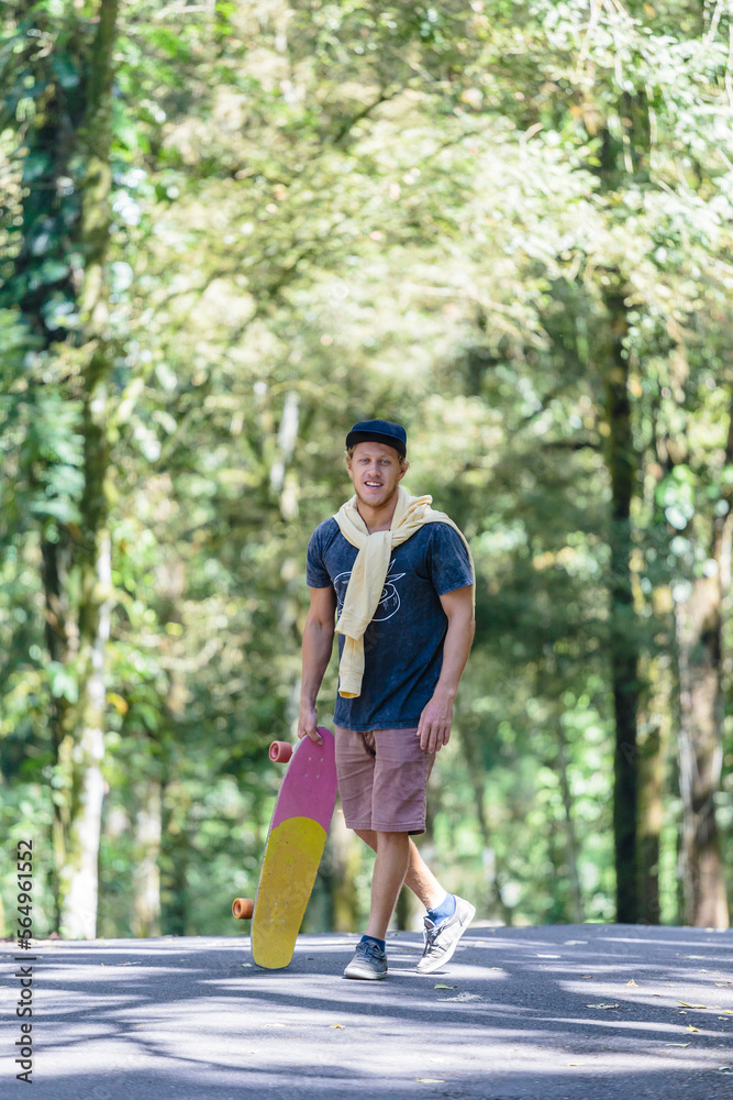 Portrait of man with skateboard standing on street, Bedugul, Bali, Indonesia Portrait of man with skateboard standing on street, Bedugul, Bali, Indonesia