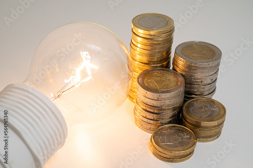 Light bulb turned off, with stacks of coins next to it. Rising electricity tariffs, energy dependency, energy sources and energy supplies.
