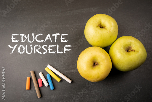 Educate Yourself Concept. Text, apples and colored pieces of chalk on a dark blackboard