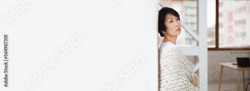 Asian woman covered with knitted plaid. Cozy winter style. portrait of dreamy smiling Asian woman in the plaid relaxing at home. banner. easonal affective disorder photo