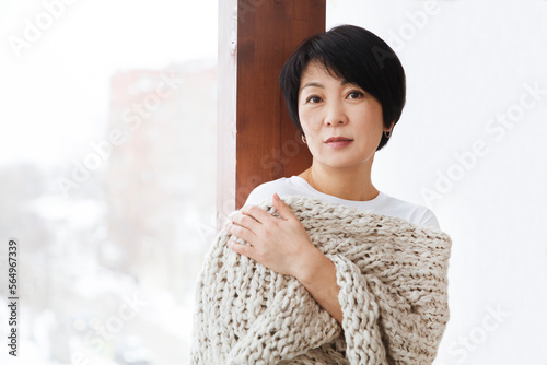 Asian woman covered with knitted plaid. Cozy winter style. portrait of dreamy smiling Asian woman in the plaid relaxing at home. banner. easonal affective disorder photo