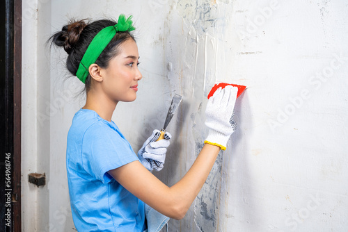Asian young housewife in a glove holding a paint scraper and paint putty photo