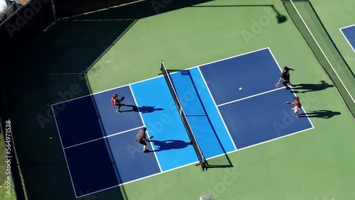 Pickleball foursome playing on sunny day hitting ball over net, aerial descending down over court photo