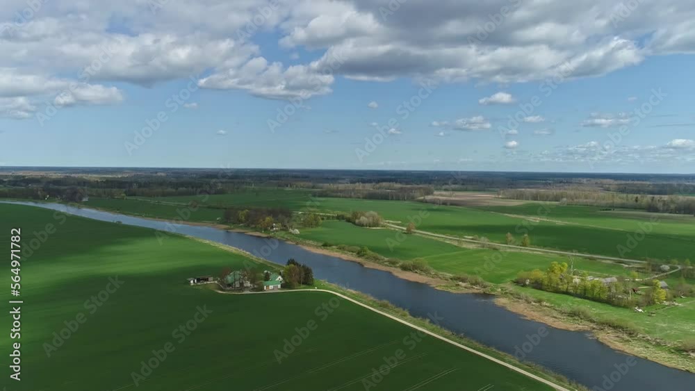 Aerial drone video shot of wide green grass field and long river in a village Aerial drone video shot of wide green grass field and long river in a village