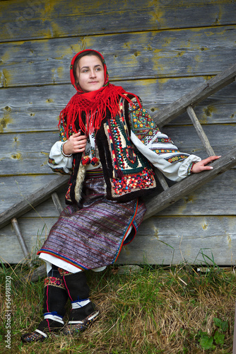 Ukrainian hutsul woman in authentic national costume sitting on a ladder near a wooden wall photo
