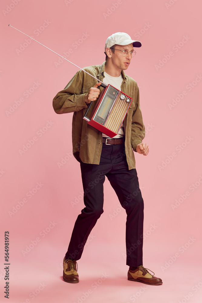 Young positive man in casual stylish clothes posing with vintage radio set, dancing, enjoying music over pink studio background. Concept of emotions, facial expression, lifestyle, retro fashion. Ad Young positive man in casual stylish clothes posing with vintage radio set, dancing, enjoying music over pink studio background. Concept of emotions, facial expression, lifestyle, retro fashion. Ad