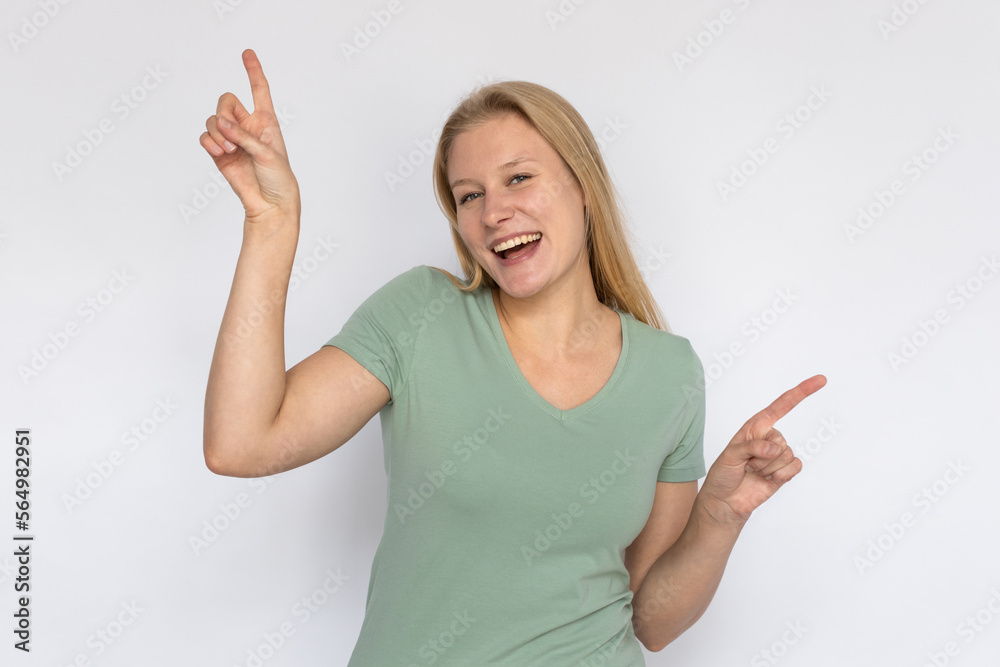 Excited young woman pointing up at ads. Portrait of happy Caucasian female model with fair hair in green T-shirt looking at camera, laughing, showing two options with fingers. Advertising concept Excited young woman pointing up at ads. Portrait of happy Caucasian female model with fair hair in green T-shirt looking at camera, laughing, showing two options with fingers. Advertising concept