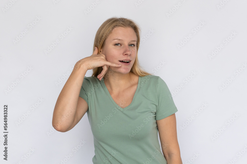 Pleased young woman showing call me sign. Portrait of happy Caucasian female model with fair hair in green T-shirt looking at camera, smiling, asking to call her. Advertising, support concept Pleased young woman showing call me sign. Portrait of happy Caucasian female model with fair hair in green T-shirt looking at camera, smiling, asking to call her. Advertising, support concept